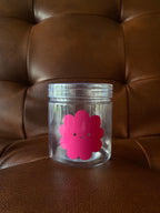Clear jar with a pink flower-shaped label on a brown leather surface