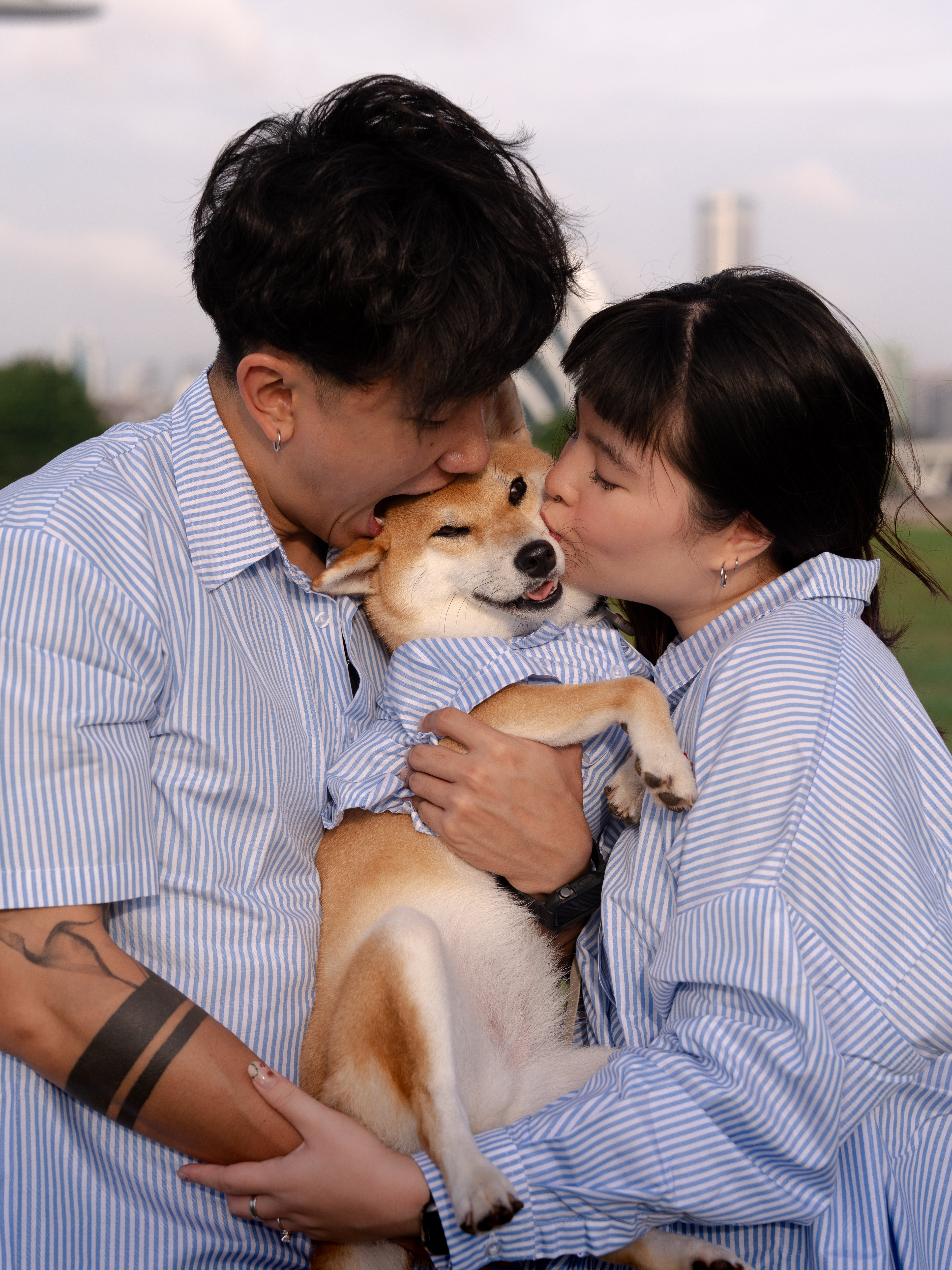 Two people in matching outfits holding a Shiba Inu dog outdoors.
