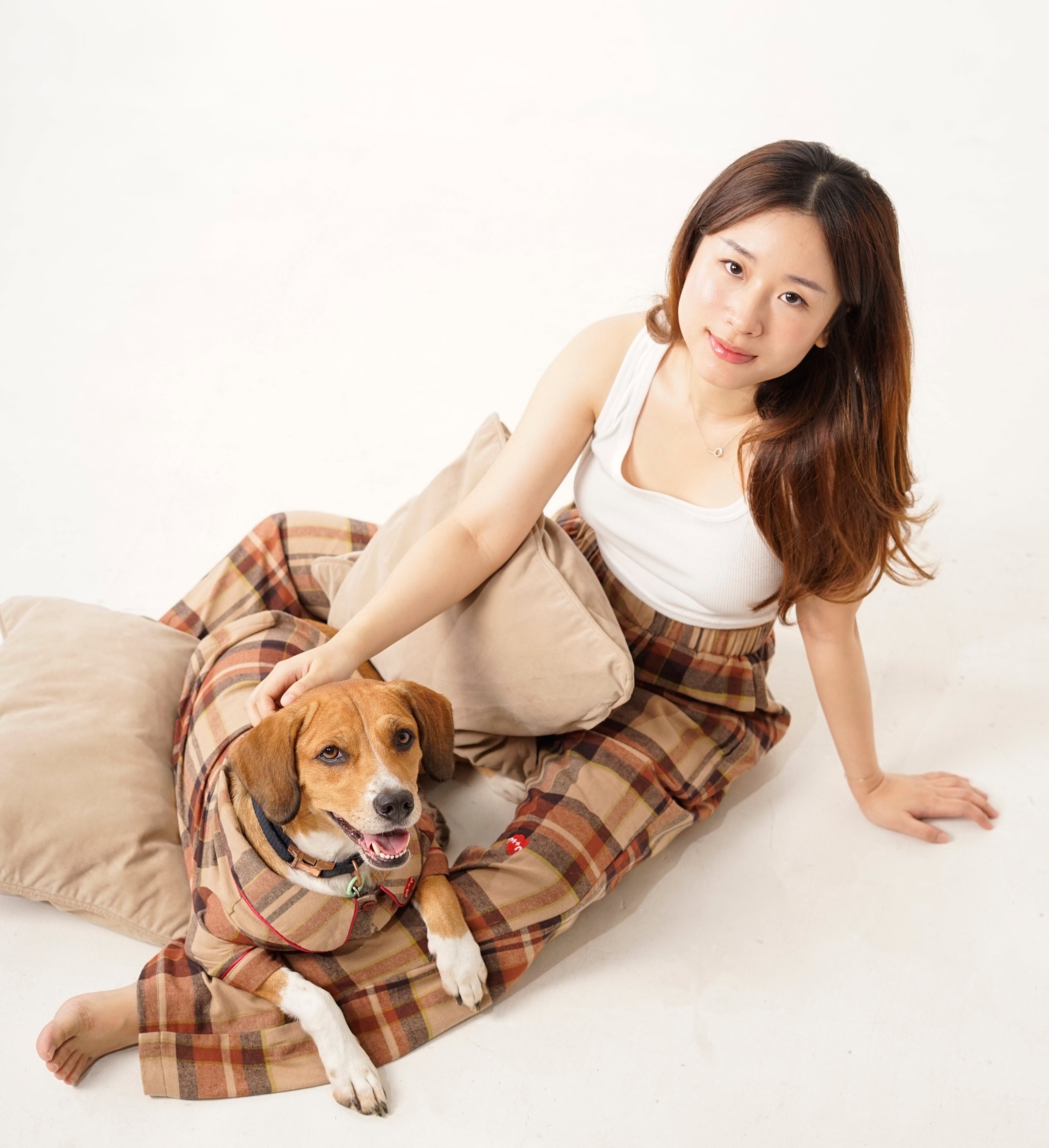 Woman in plaid skirt sitting on a white surface with a dog wearing a coat.