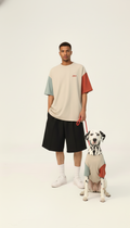 Man wearing a color-blocked t-shirt and shorts with a dog on a leash against a white background