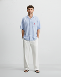 Man wearing a light blue striped shirt and white pants on a gray background