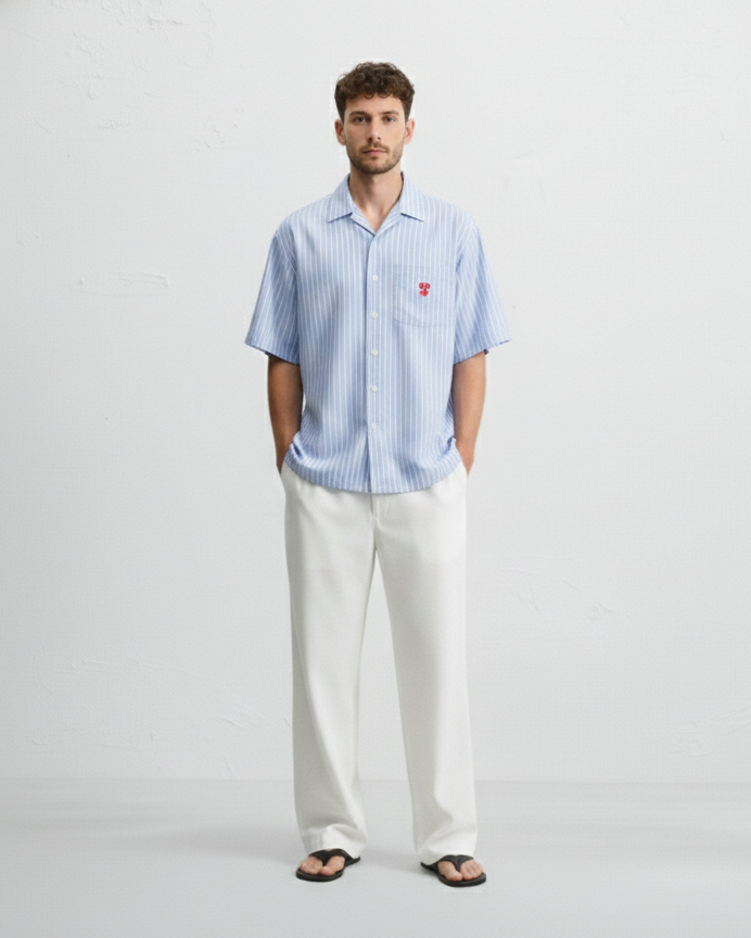 Man wearing a light blue striped shirt and white pants on a gray background