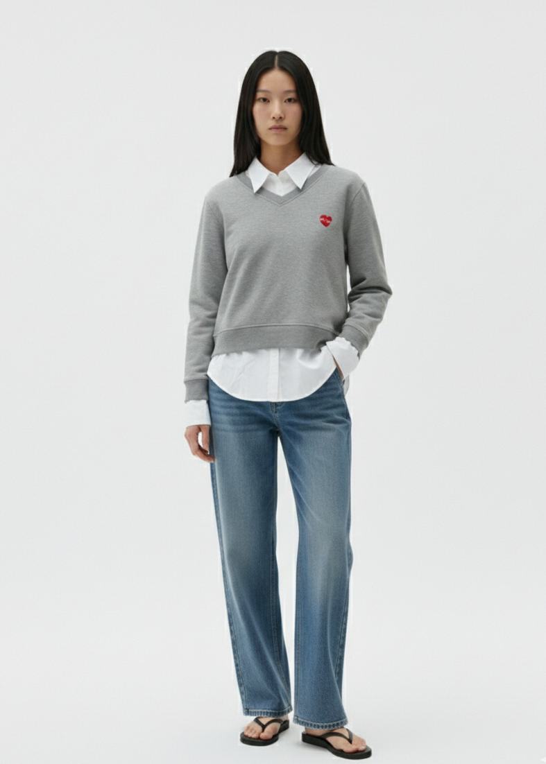 Person wearing a gray sweater with a red heart emblem, white shirt, and blue jeans on a white background