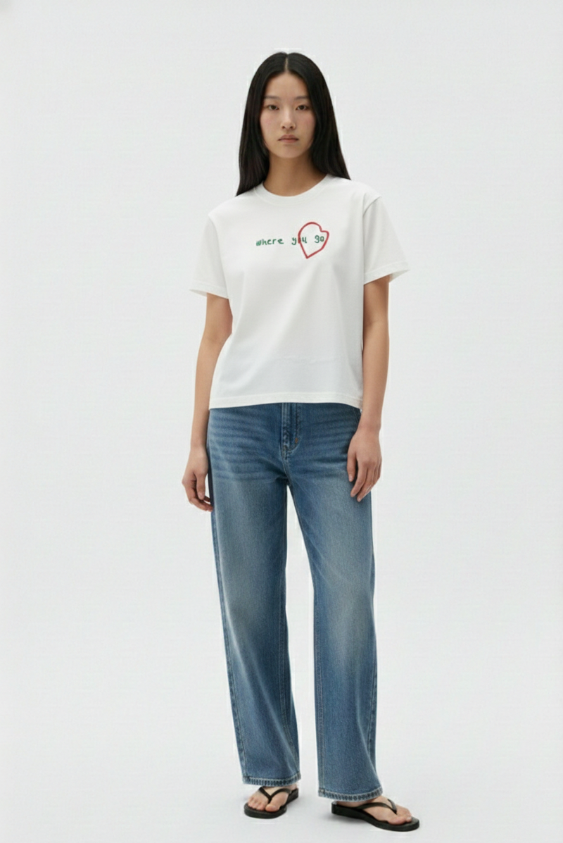 Person wearing a white t-shirt with a red heart design and blue jeans on a white background