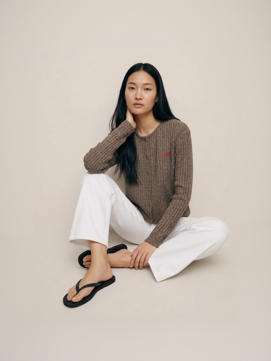 Woman sitting on the floor wearing a brown sweater and white pants against a beige background