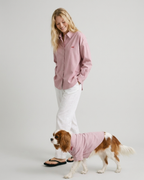 Woman and dog wearing matching pink shirts on a plain background