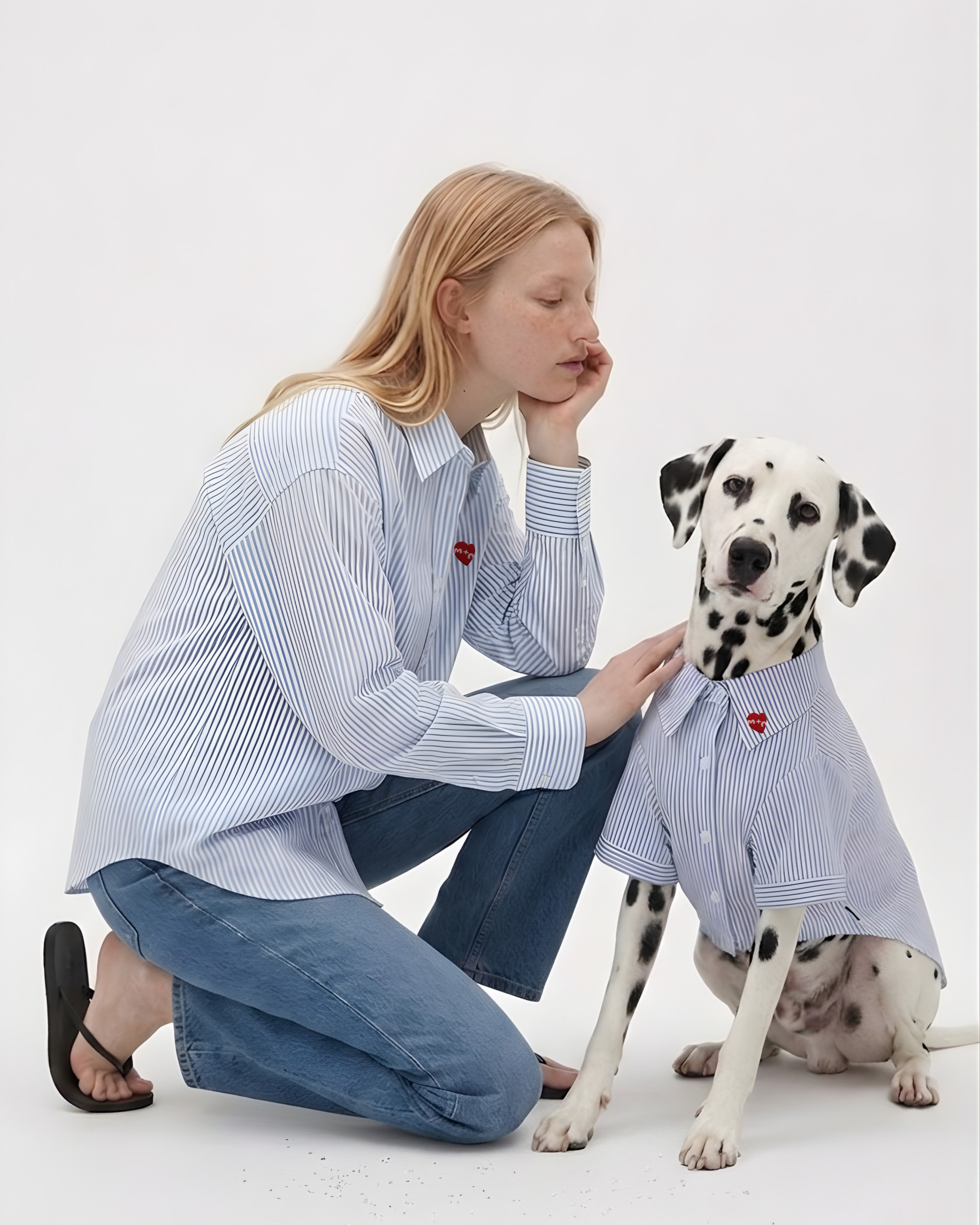 Person and Dalmatian dog wearing matching blue striped shirts on a white background