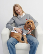 Woman sitting on a white chair with a brown dog wearing a matching sweater.