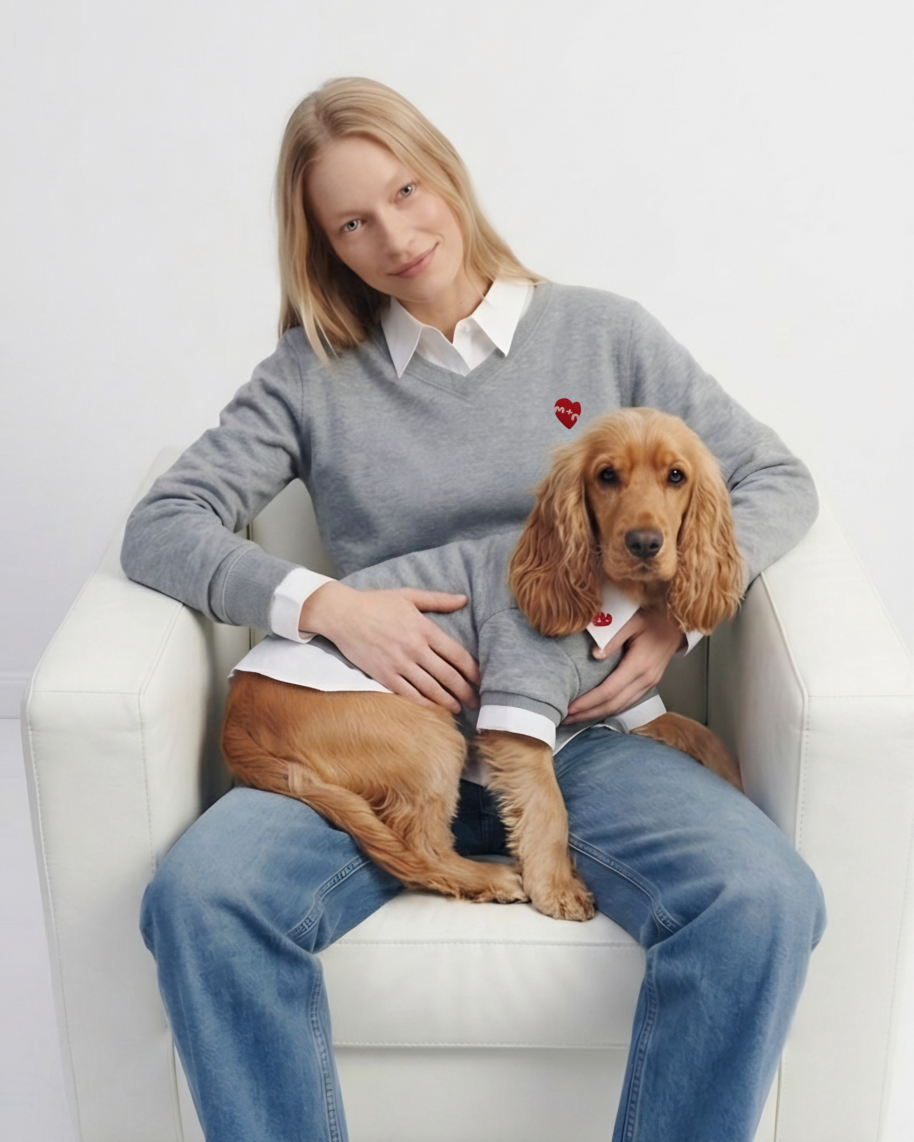 Woman sitting on a white chair with a brown dog wearing a matching sweater.