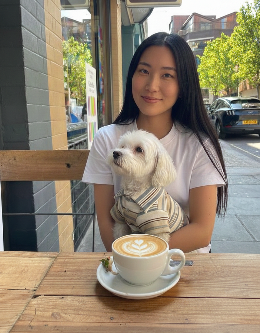 Woman holding a small white dog with a cup of coffee at an outdoor cafe.